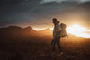 Man with a backpack standing in a field during sunset with mountains in the background