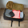 Open suitcase with clothes and a black item on a wooden floor