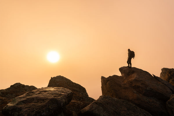 Person standing on a rocky outcrop with the sun setting in the background
