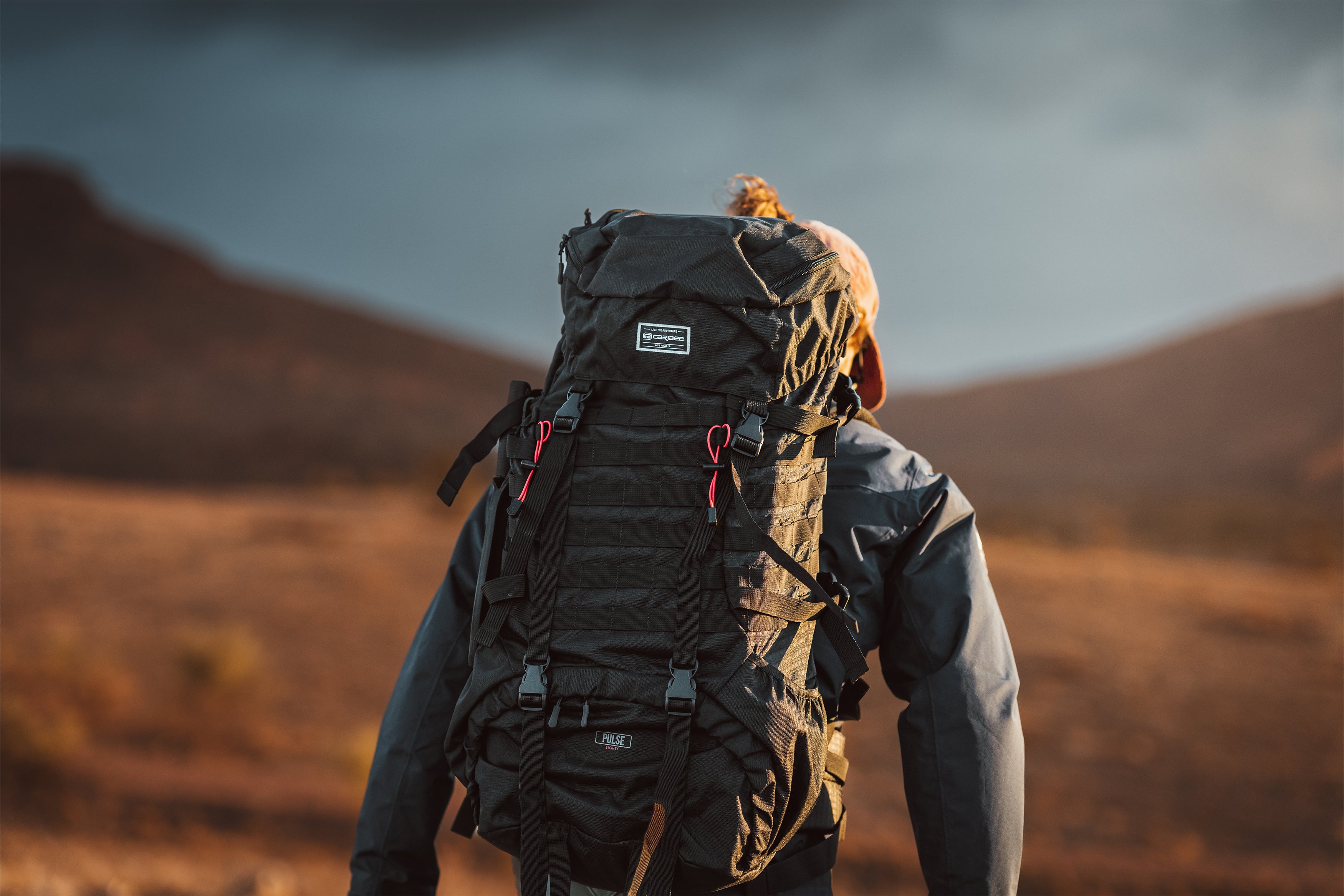 Person with a large black Caribee rucksack walking through a desert landscape