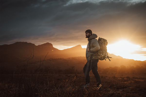 Man with a backpack standing in a field during sunset with mountains in the background