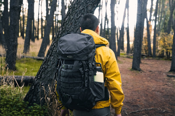 Person wearing a black Caribee rucksack and yellow jacket in a forest
