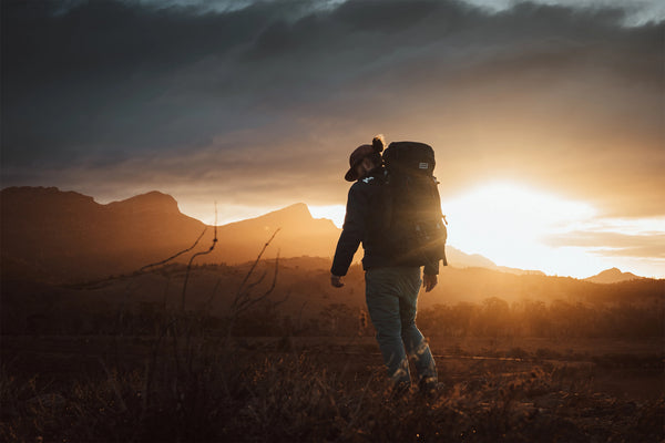 Person with a Caribee rucksack backpack walking towards a sunset in a mountainous landscape