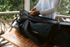 Person opening a black waterproof bag with a visible Caribee logo on a wooden table outdoors with dive fins
