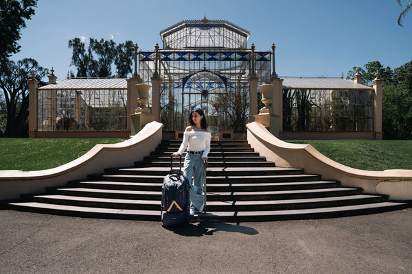 Woman with Caribee suitcase standing on steps in front of a large glass building.