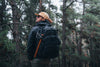 Person with a Caribee Op's backpack in black with axe attached standing in a forest